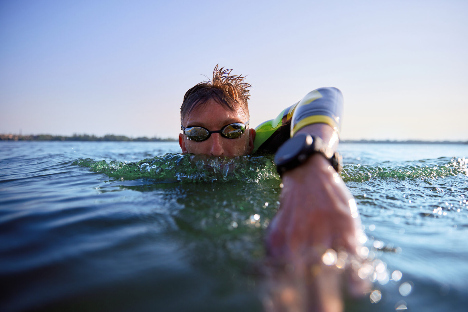 Front crawl swim type. Man, athlete in goggles swimming into water, river, training outdoors. Concept of professional sport, triathlon preparation, competition, athleticism