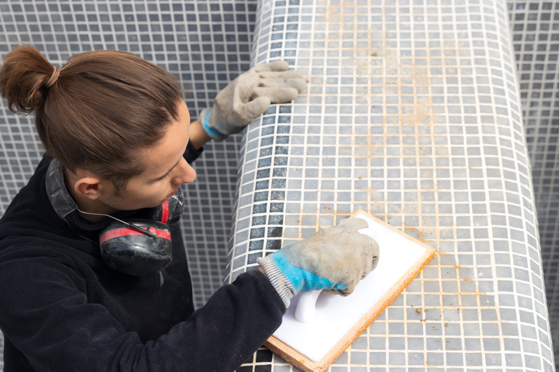 View from above of hypster man working and finishing putting blue tiles on a constrcution work