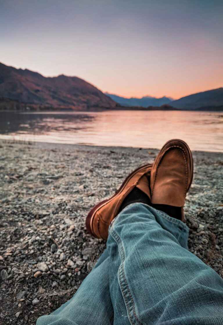 A peaceful moment at sunset with legs crossed on a lake shore, enjoying leisure time.